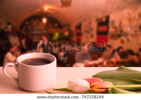 Tea cup with tulips on the wooden table opposite blurred background. Collage. Selective focus. Toned.