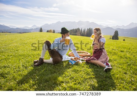 Couple in traditional clothes, Dirndl for Oktoberfest drinking beer and with pretzel from Germany, Munich, Bavaria
