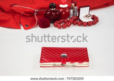 red lacquered purse on the background of a set of objects of red color: perfume, lipstick, coat, perfume, costume jewelry, ring