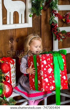 Beautiful happy girl unwrap christmas present box on holiday morning in beautiful room interior. Female child open Xmas gift near decorated fir tree. Winter holidays concept