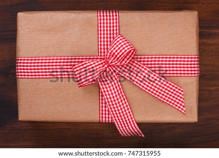 Wrapped gift box with red and white checkered ribbon bow on a dark walnut wood, top view, close up