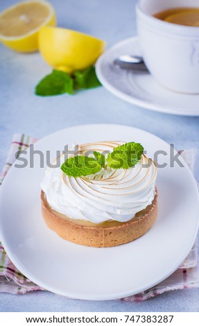 Delicious Lemon tart tartlet with meringue and mint in white plate on blue stone concrete table background. Copy space