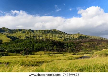 Color outdoor idyllic landscape panorama  photography with a view over grassland and a creek towards the Drakensberge mountains, South Africa on a sunny day with blue sky and some clouds 
