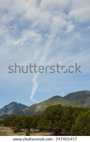 An airplane contrail over the mountains of Colorado looks suspiciously like a rope tornado.  But the cumulous clouds around it give away its true definition. 