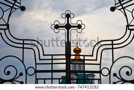 openwork gate of a church with an orthodox cross against a gray sky