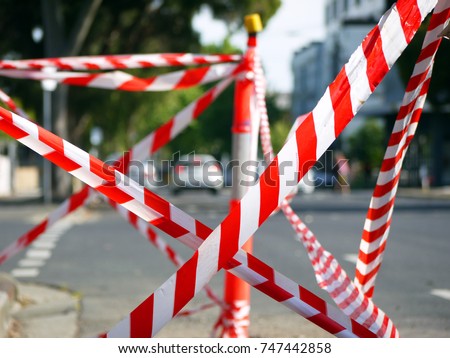 White and red road safety barricade tapes with a blurry street view.