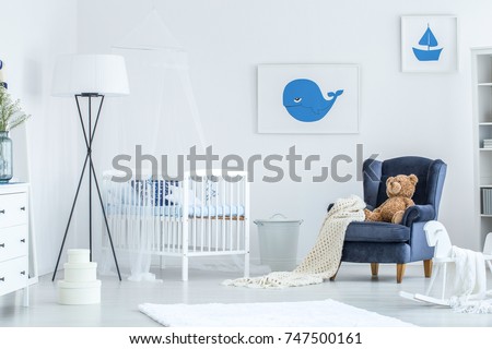 Lamp next to bed in white and blue baby's bedroom with bear toy on armchair and rocking horse