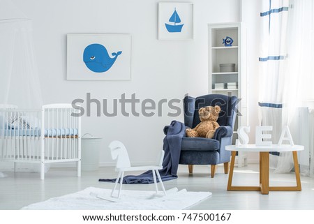 Wooden table, rocking horse, bear toy on armchair and bed in white marine kid's bedroom