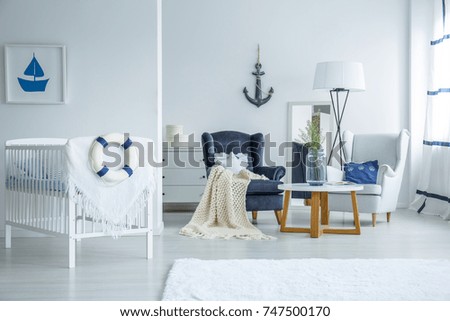 Lifebuoy on kid's bed and posters on walls in marine interior with armchairs at table with vase and lamp