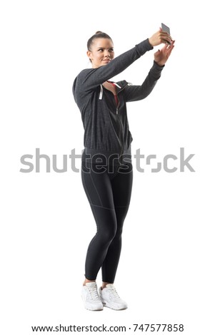 Relaxed young pretty athletic woman in sportswear taking selfie looking at phone. Full body length portrait isolated on white background. 