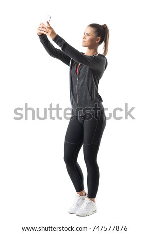 Side view of young confident proud active sporty woman taking selfie looking at phone. Full body length portrait isolated on white background. 
