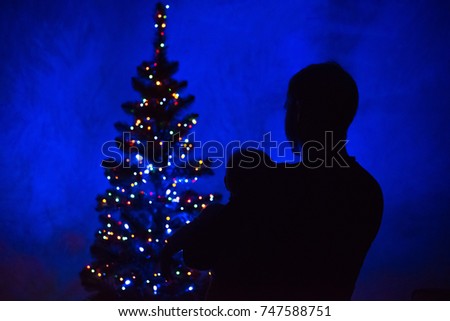 A silhouette of a father holding a baby in his arms and looking at the Christmas tree lights. New Year's day eve picture.
