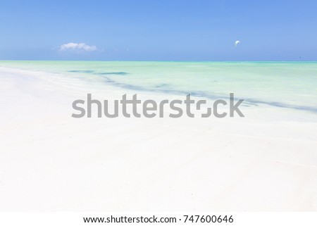 Solitary kite surfer kite surfing on picture perfect white sandy beach with turquoise blue sea, Paje, Zanzibar, Tanzania. Copy space. Horizontal composition.