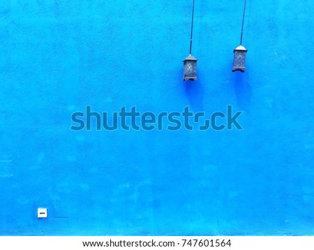 vintage blue paint cement wall and small white plug below the left, two birdcage lamp hang on, simple elegant decoration creative design concept, modern garden home style, copy space for your text