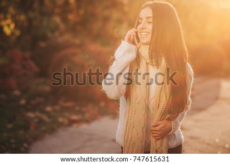 Woman using smartphone in fall. Autumn girl having smart phone conversation in sun flare foliage. Portrait of Caucasian model in forest in fall colors.