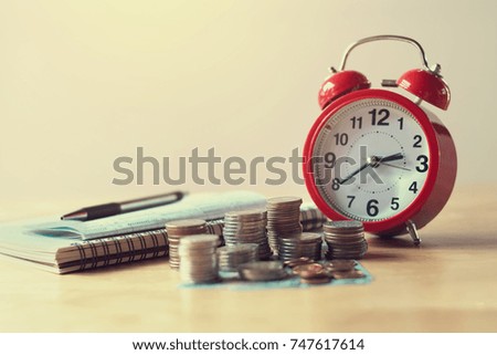 coins stack and red alarm clock with pen, notebook for banking and finance concept