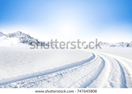 Winter Background of foreground of road covered with snow and ice. In the background, the arctic landscape of the mountains with the beautiful blue sky.