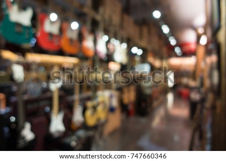 Blurry background with many electric guitars hanging on the showcase at side wall in the musical showroom and and bokeh of ligthing
