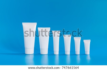 White cosmetic tube collection arranged small large on blue background. Abstract plastic containers different size capacity, blank template packaging design. copy space photo.