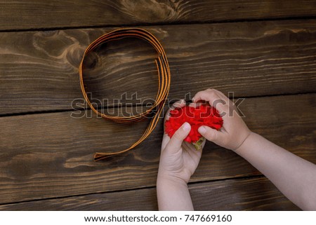 Red carnations and St. George ribbon on wooden background/St. George ribbon - the symbol of the great Victory/Victory Day/Flower/ carnation in the hands of a child. Top view