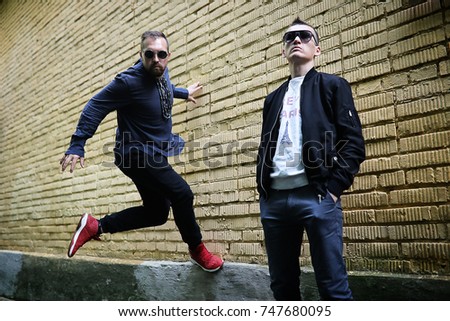 Two men in sunglasses against a brick wall background
