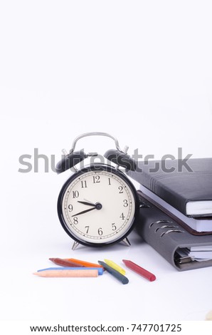 Stack of book with ticking vintage clock and colorful crayon on white table.negative space for text