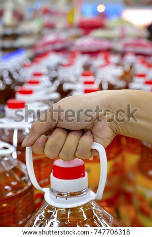 Female hand holding cooking oil bottle at supermarket, selective focus.