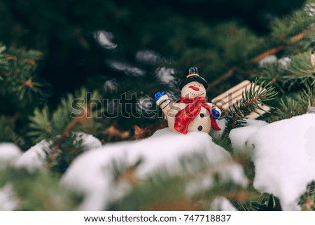 Christmas decoration small snowman with red scarf and miniature wooden sled on the branch. Winter holidays.
