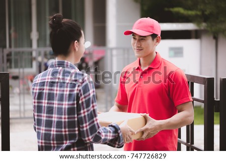 Young logistic career concept. Happy delivery man giving his package to customer at home. Taken in real house. Asian chinese fit man in red polo shirt and jeans with red hat in his early twenties. Royalty-Free Stock Photo #747726829