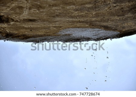 Droplets of rain water falling from natural rocks in a cave against the cloudy sky. Wet weather, misty air, high humidity, moisture.