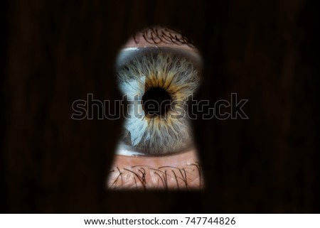 Female blue eye looking through the keyhole. The concept of voyeurism, curiosity, Stalker, surveillance and security Royalty-Free Stock Photo #747744826