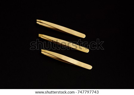 Close up set of gold tweezers on black background 