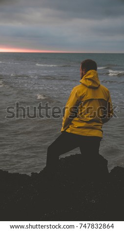 Adult Caucasian male in yellow raincoat enjoying the view of a sunset over the sea