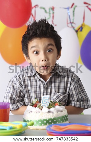 Boy with in front of  birthday cake with surprise expression