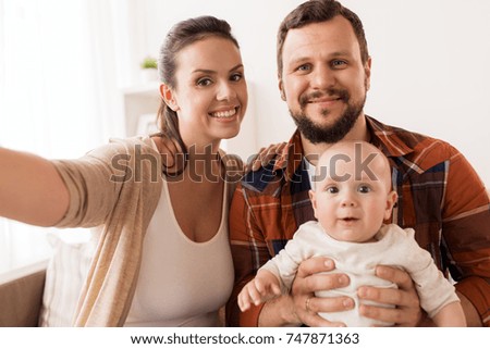 family, parenthood and people concept - happy mother and father with baby taking selfie at home