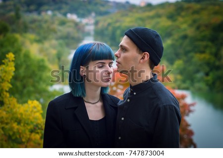 Gothic couple outdoors love story. Man and blue hair girl at black clothes at green river background