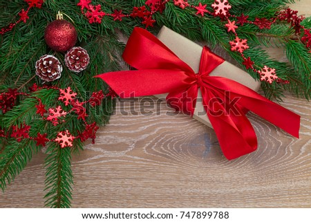 Christmas present, tied with a red ribbon, lies next to a spruce branch on a wooden floor