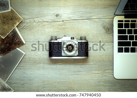 Flat view of vintage rangefinder film photo camera, with some unidentified pictures and notebook on a rustic wooden table. Concept background for working in digital design and post production editing 