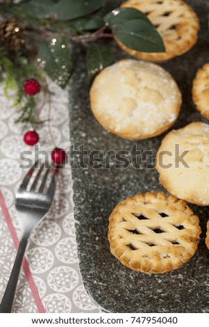 Selection of fresh frosted mince pies on a tray with festive christmas decorations on a country table