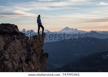 Adventurous man is standing on top of the mountain and enjoying the beautiful view during a vibrant sunset. Taken on top of Cheam Peak in Chilliwack, East of Vancouver, BC, Canada. Royalty-Free Stock Photo #747991465
