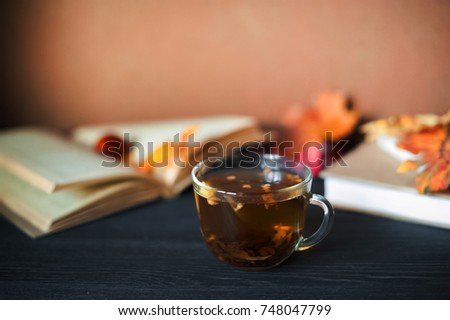 
Winter photography with books, a cup of tea, fallen yellow leaves, chestnuts. On a black wooden background lie books and a cup of tea. A card with a place for your text.
