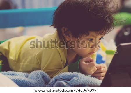 asian children watching tablet  / playing phone and looking at cartoon / kid play tablet
