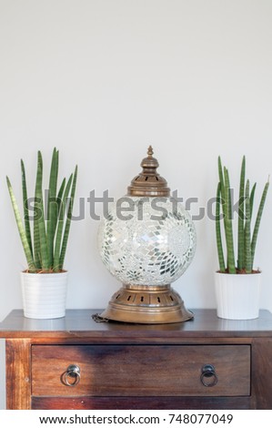 Plants and a decorative Greek mosaic lamp on a wooden drawer in a relaxed home office interior in Finland.
