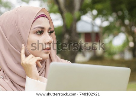 Young Muslim woman using laptop at the park. Close up, Muslimah concept. 
