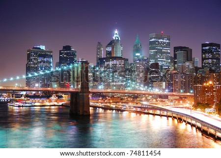 New York City Manhattan skyline and Brooklyn Bridge with skyscrapers over Hudson River illuminated with lights and busy traffic at dusk after sunset.