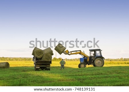 a tractor on a farm field harvests crops / farmland Royalty-Free Stock Photo #748139131