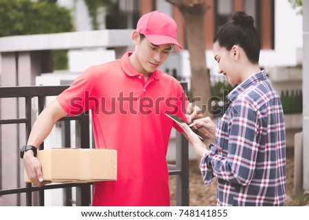 Young logistic career concept. Happy delivery man giving his package to customer at home. Taken in real house. Asian chinese fit man in red polo shirt and jeans with red hat in his early twenties. Royalty-Free Stock Photo #748141855