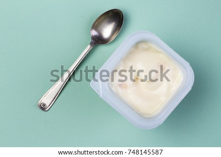 Healthy yellow fruit flavored yoghurt with natural coloring in plastic cup isolated on green background with small silver spoon - top view Royalty-Free Stock Photo #748145587