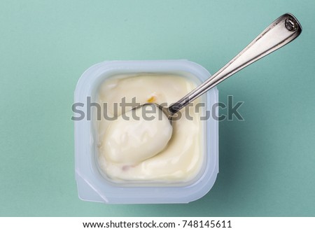 Healthy peach - apricot fruit flavored yoghurt with natural coloring in plastic cup isolated on green background with small silver spoon - top view Royalty-Free Stock Photo #748145611