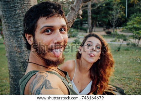 Handsome couple taking selfie photo in the outdoor tropical park on sunset, show the 
tongue